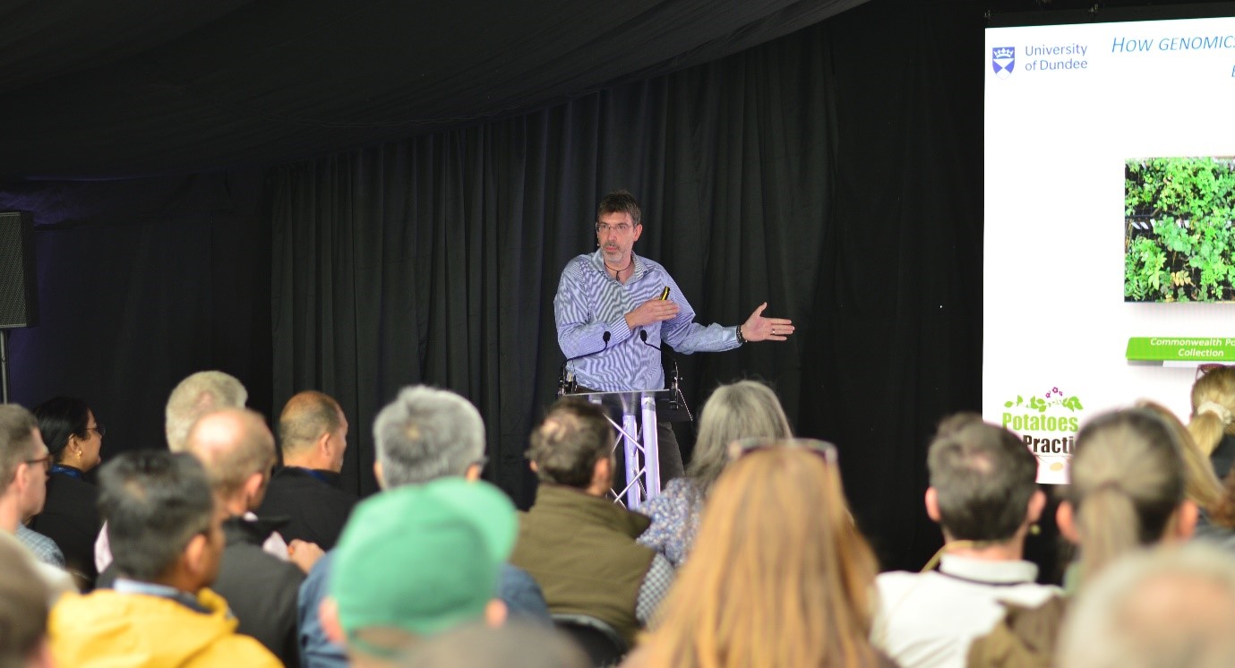 Ingo Hein (hutton Scientist) speaking to seated crowd at a lectern in front of large LED screen and blacked out background