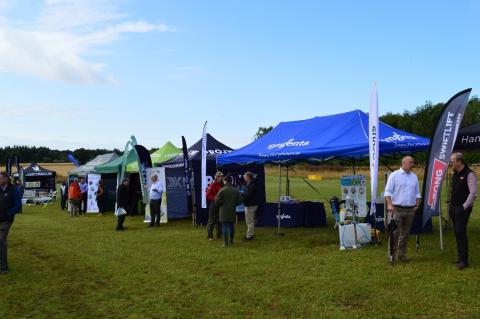 Exhibitor gazebos in a green field. Attendees and Exhibitors engaging. 