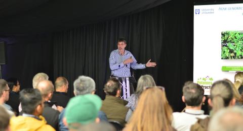 Ingo Hein (hutton Scientist) speaking to seated crowd at a lectern in front of large LED screen and blacked out background